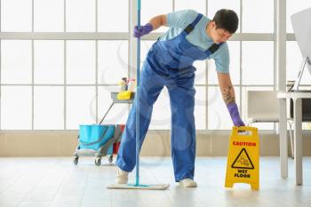 Male janitor mopping floor in office�