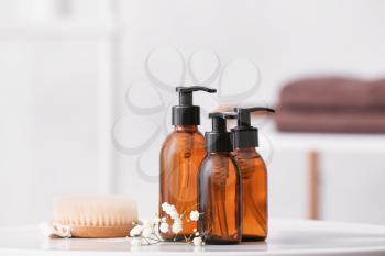 Different shower gels, brush and flowers on table in bathroom�