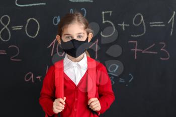 Little girl wearing medical mask near school blackboard�