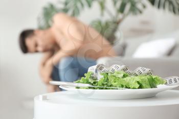 Young man suffering from anorexia and plate with salad at home 