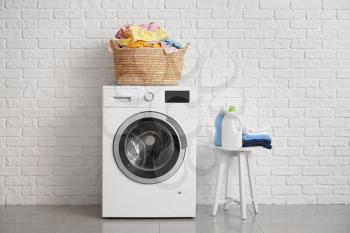 Washing machine and basket with laundry near white brick wall�