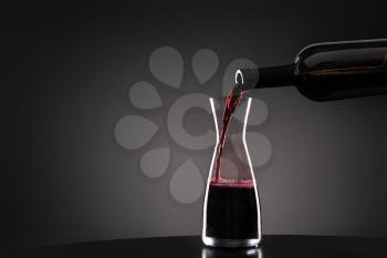 Pouring of tasty wine from bottle into glass on dark background�