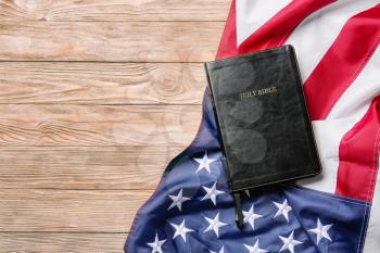 Holy Bible and USA flag on wooden background�