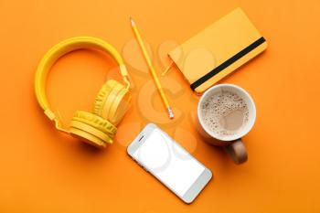Modern mobile phone with headphones, notebook, cup of coffee and pencil on color background 