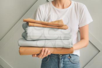 Woman with stack of clean bed sheets on light background�