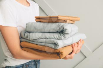 Woman with stack of clean bed sheets on light background�