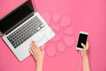 Female hands with modern laptop and mobile phone on color background�