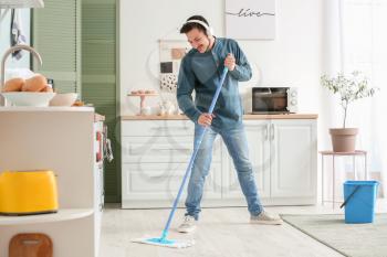 Handsome young man mopping floor in kitchen�