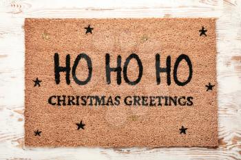 Door mat with Christmas greeting on wooden background�