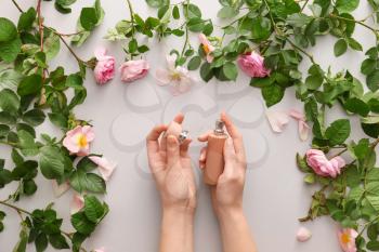 Female hands with perfume and flowers on light background�