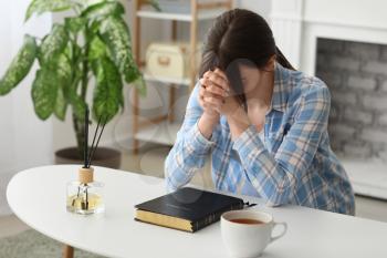 Young woman with Bible praying at home�