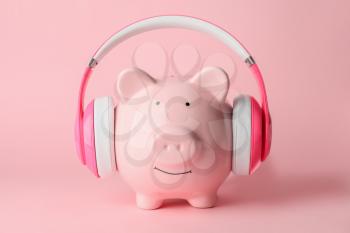 Piggy bank with headphones on color background�