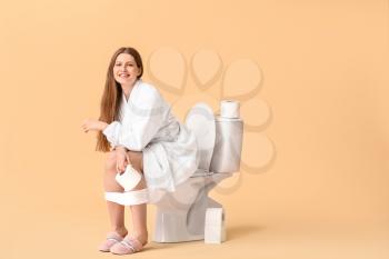 Young woman sitting on toilet bowl against color background�