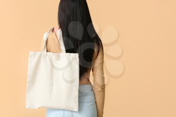 Young woman with eco bag on color background, back view�