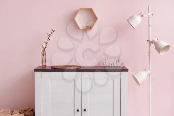 Modern chest of drawers with lamp near color wall in room�