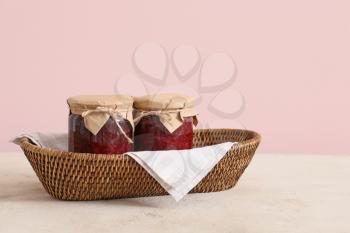 Wicker basket with jars of jam on color background�