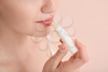 Beautiful young woman with lip balm on color background, closeup�
