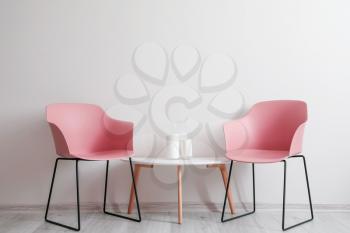 Stylish armchairs with table near light wall�
