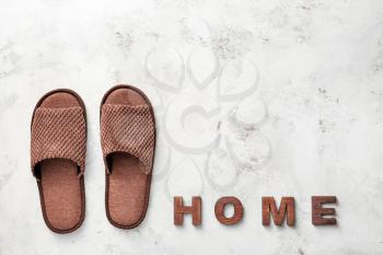 Pair of soft slippers and word HOME on light background�