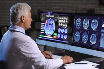 Senior neurologist with MRI scan of human head on screen of computer monitor in clinic�