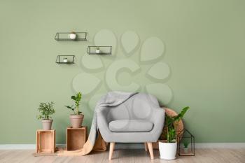 Interior of room with stylish armchair and houseplants near color wall�