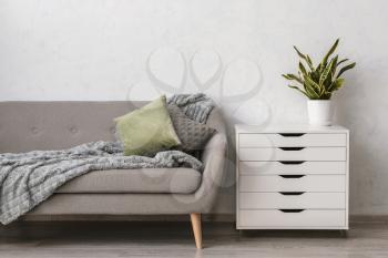 Modern chest of drawers with sofa and houseplant near light wall in room�