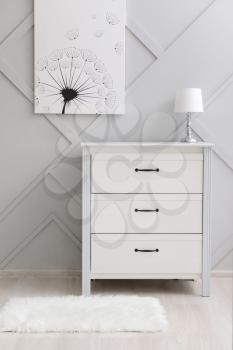 Modern chest of drawers with lamp near grey wall in room�