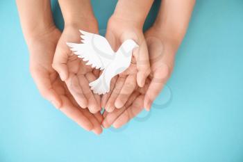 Hands of family with paper dove on color background�