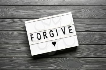 Board with word FORGIVE on wooden background�