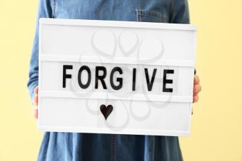 Woman holding board with word FORGIVE on color background, closeup�