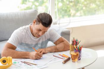 Young man coloring pictures at home�