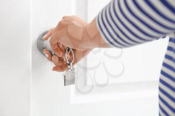 Woman using key to open door indoors�