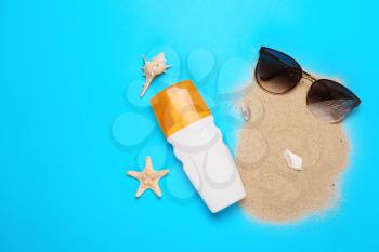 Stylish sunglasses with sunscreen and sand on color background�