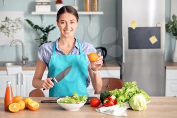 Beautiful young woman making vegetable salad in kitchen�