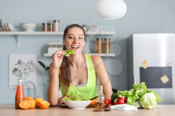 Beautiful young woman eating vegetable salad in kitchen�