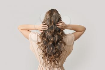 Beautiful young woman with stylish hairdo on grey background, back view 