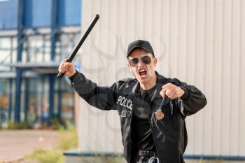 Aggressive police officer with baton outdoors�