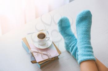Female legs in socks on table with books and cup of coffee at home. Concept of day off�