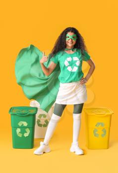 Woman dressed as eco superhero with trash bins showing thumb-up gesture on color background�