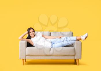Young woman relaxing on sofa against color background�