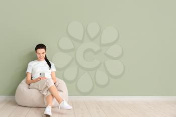 Young woman with mobile phone relaxing on beanbag near color wall�