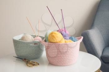 Wicker baskets with knitting yarn on table in room�