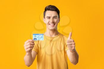 Young man with driving license showing thumb-up on color background�