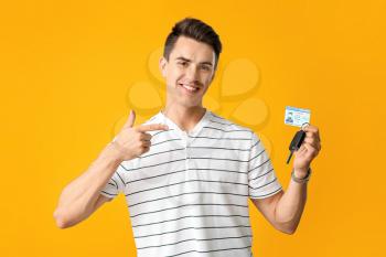 Young man with driving license and car key on color background�