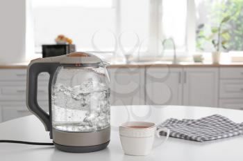 Modern electric kettle and cup of tea on kitchen table�