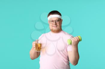 Overweight man with glass of beer and dumbbell on color background. Weight loss concept�