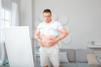 Sad overweight man near mirror at home. Weight loss concept�