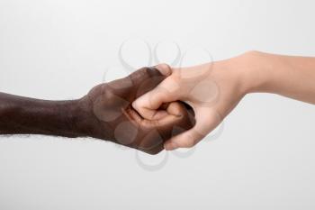 Caucasian woman and African-American man holding hands together on light background. Racism concept 