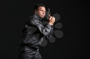 African-American police officer with gun on dark background�