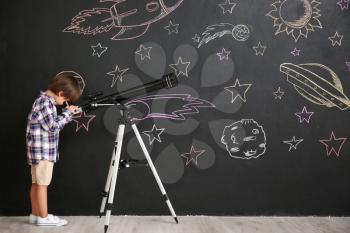 Cute little boy watching in telescope on black wall with drawn space�